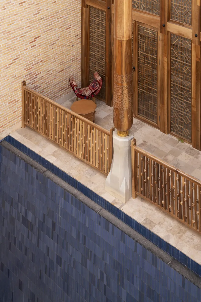 Overhead view of carved timber screens and column base around a tiled reflecting pool at dusk