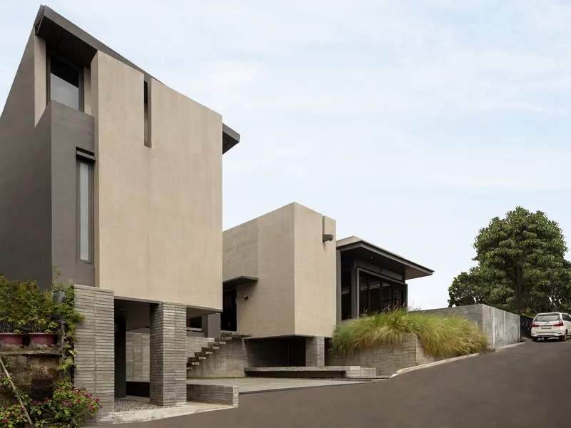 Angled view of the concrete volumes linked by external stairs with ornamental grasses and a tree