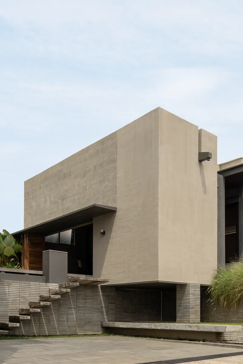 Cantilevered concrete volume above a water feature with stone steps under overcast skies