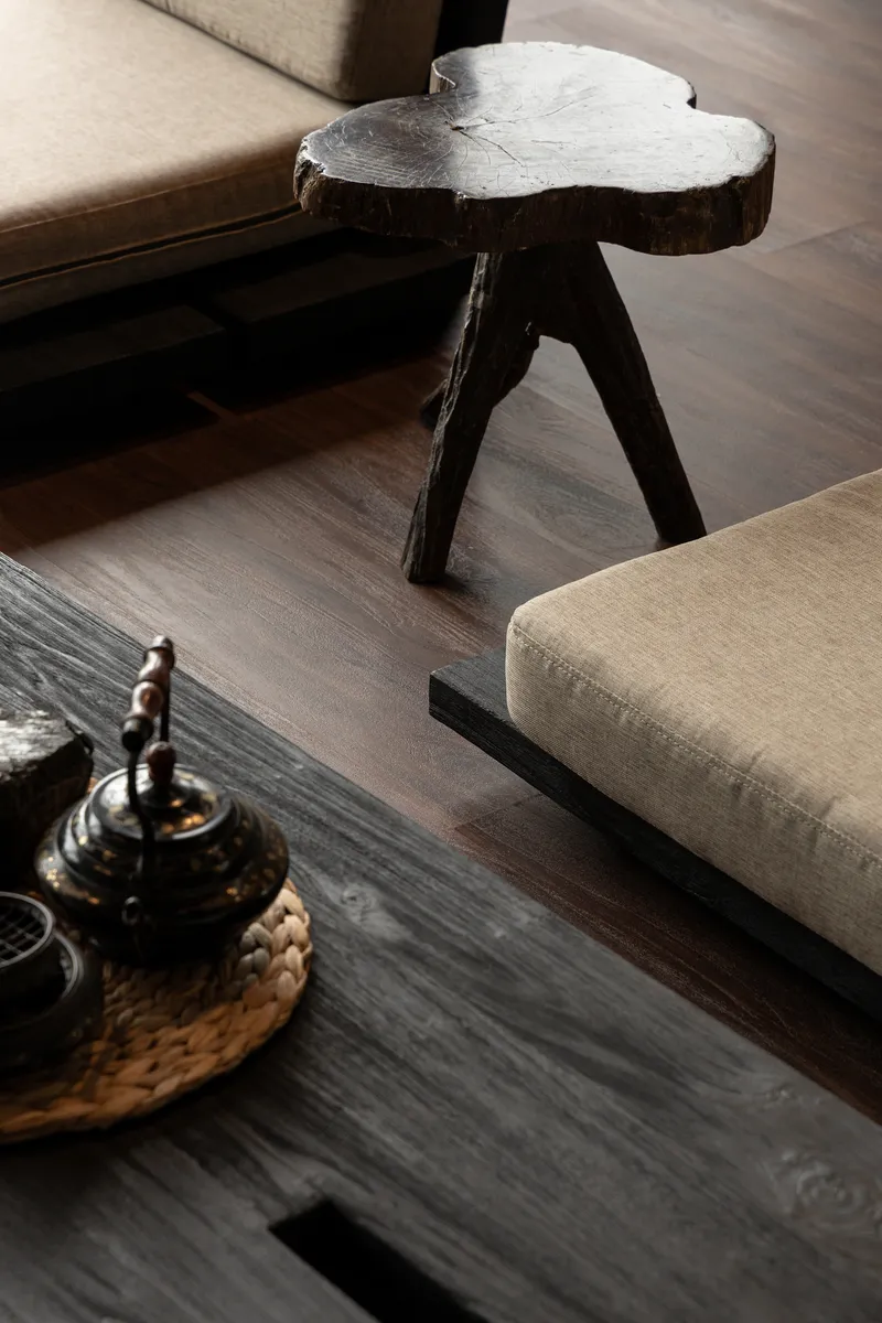 Live-edge timber side table on dark wood flooring beside upholstered seating and metal teapot