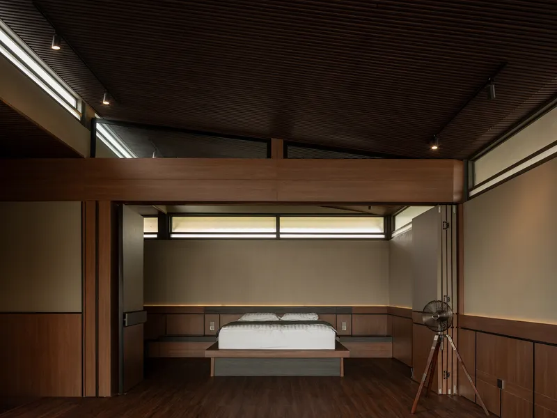 Bedroom with timber bed platform below mezzanine and horizontal clerestory windows with slatted ceiling