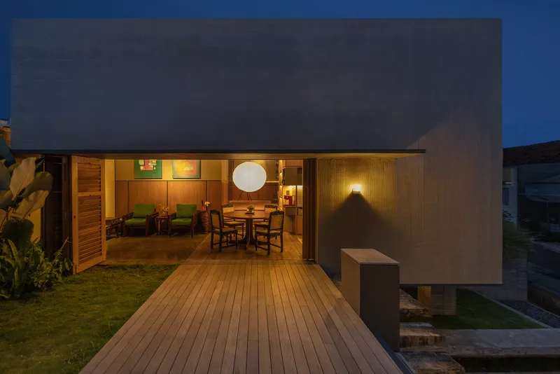 Timber deck connecting concrete wall to glazed living pavilion with sphere pendant at night