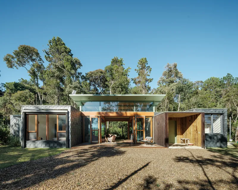 Frontal view of the linked pavilions with timber cladding and gravel forecourt under a clear blue sky