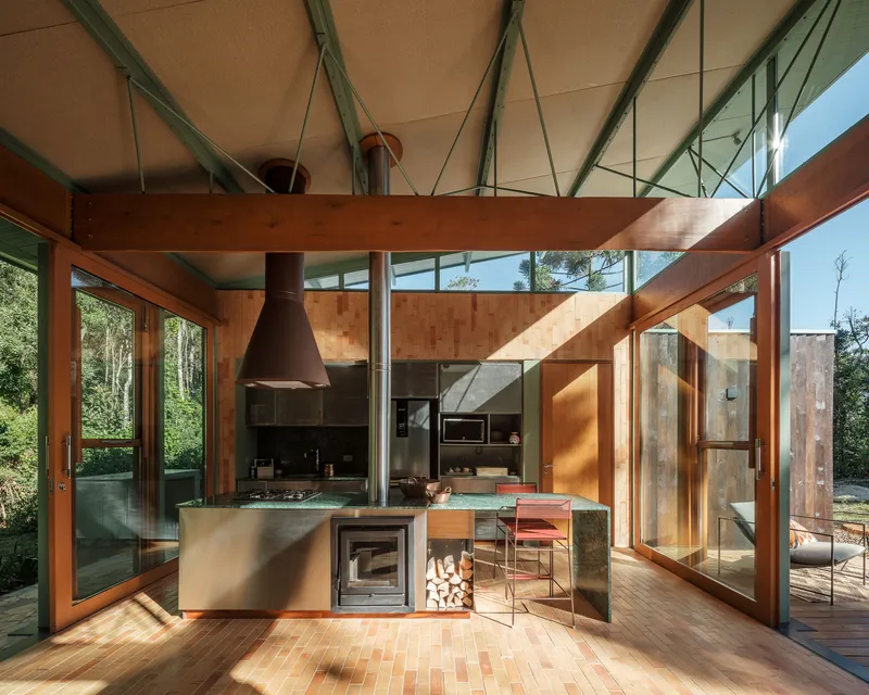 Open kitchen with steel island, timber beams and glazed walls admitting afternoon sunlight