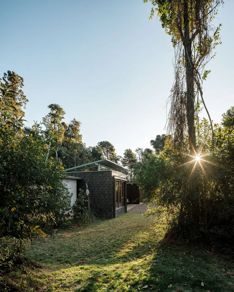 Gabled pavilion with concrete block walls glimpsed through forest clearing at sunset