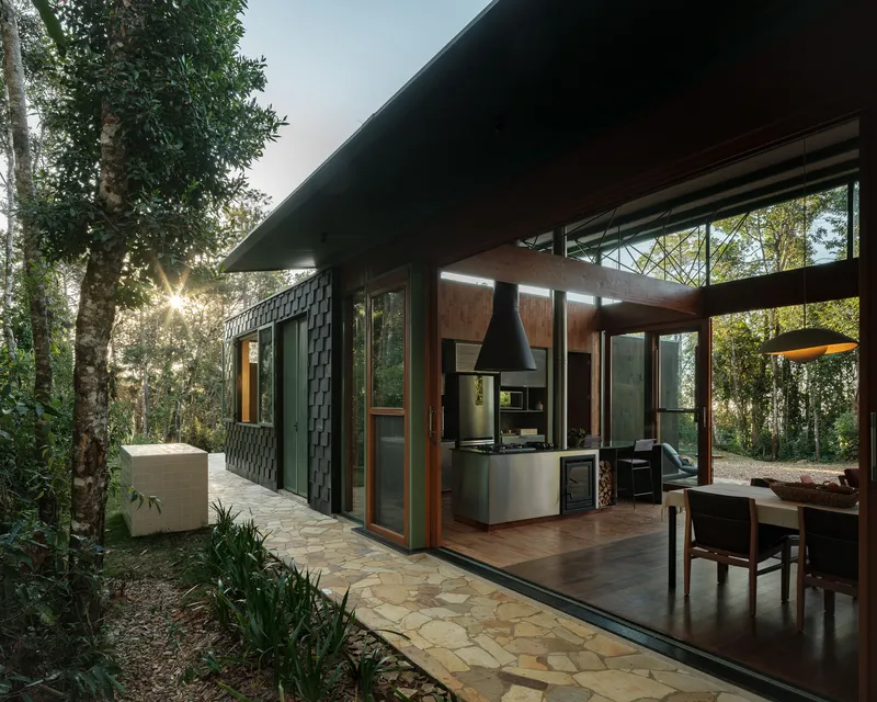 Covered terrace with timber framing and stone paving opening to a kitchen beneath a deep eave at dusk