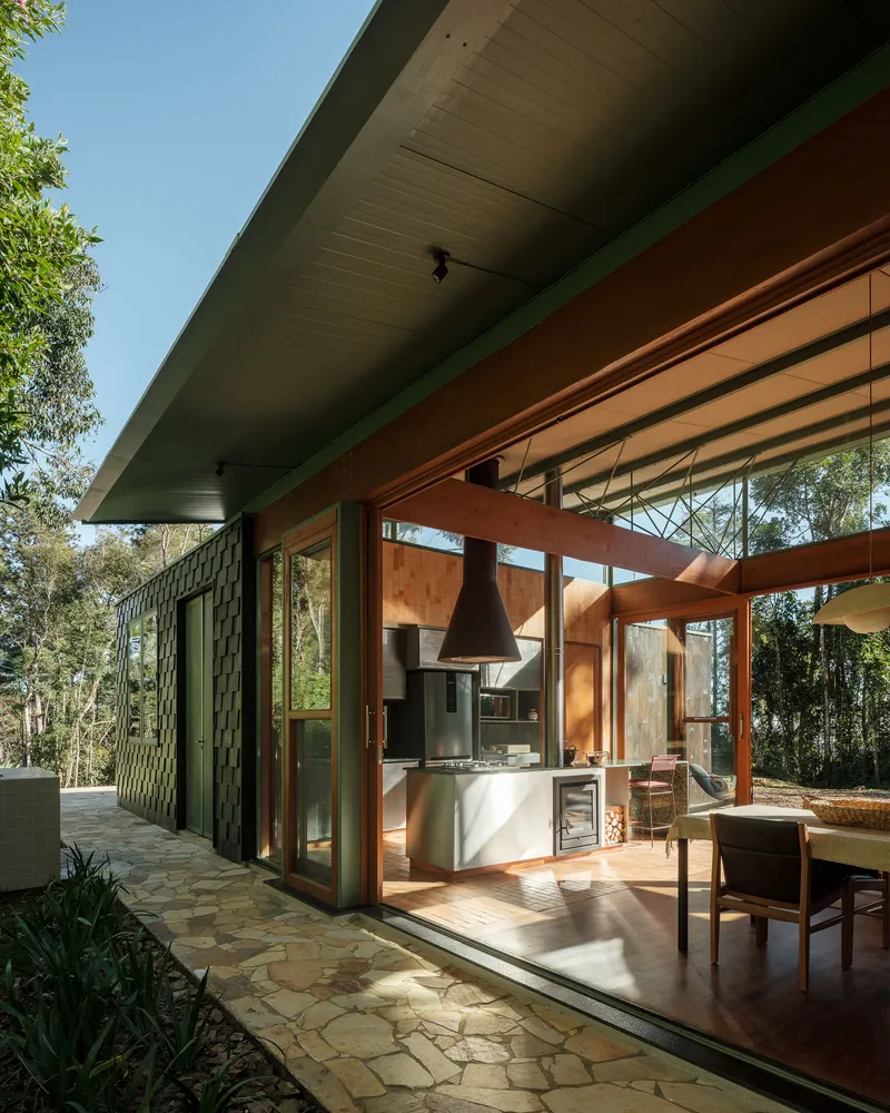 Exterior view showing exposed timber beams and green-trimmed overhang above glass walls framing the kitchen