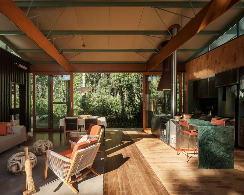 Open living and kitchen space with timber beams and green-veined stone island under morning sunlight