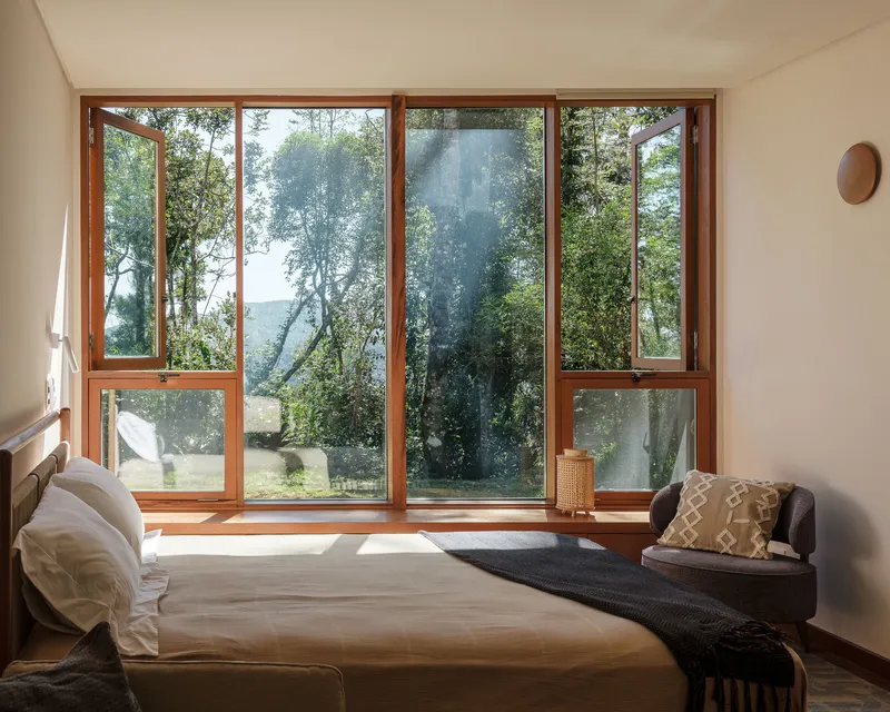 Bedroom with full-height glazed doors framing views of trees and filtered daylight