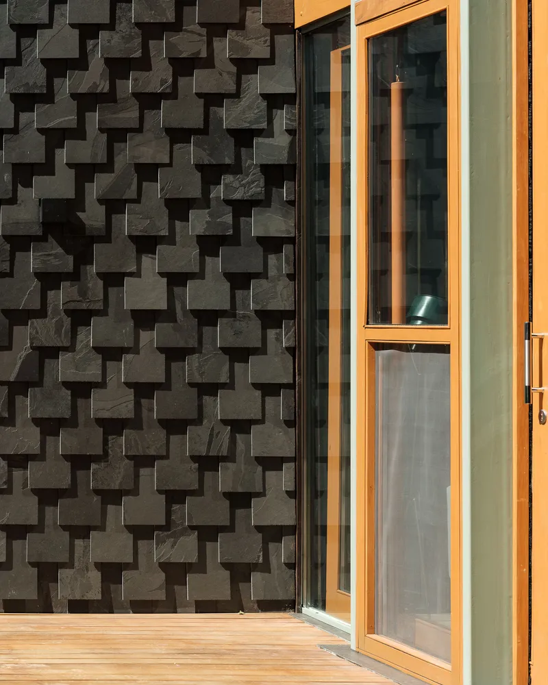 Close-up of basket-weave patterned concrete block wall meeting timber-framed glass door in afternoon light