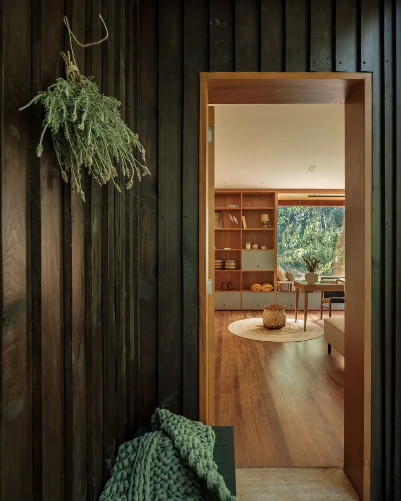 View through timber doorway into living room with built-in shelving and dried herbs hanging on dark vertical planks