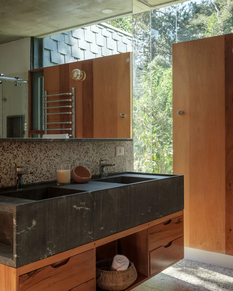 Bathroom vanity with black stone sink and timber cabinetry beneath terrazzo backsplash and exposed concrete ceiling