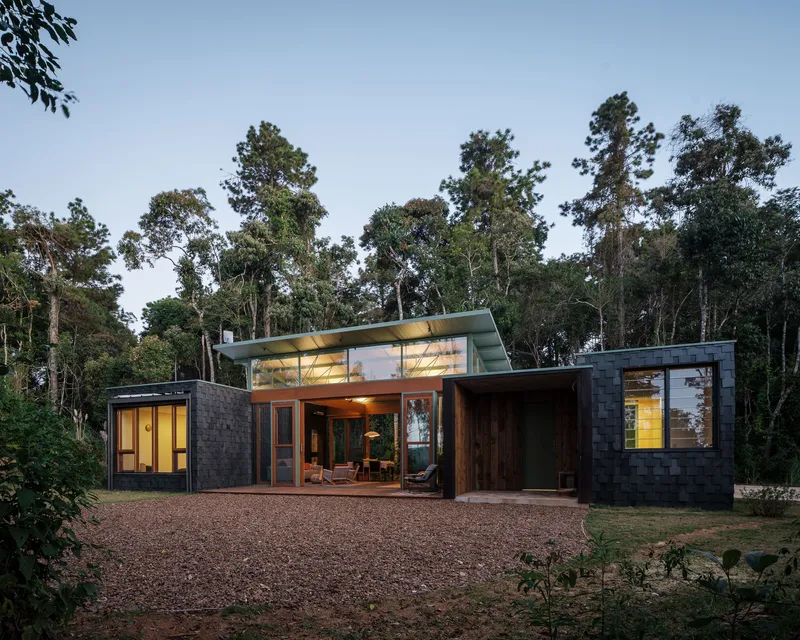 Exterior view of the single-story pavilion with lifted roof among tall trees at dusk