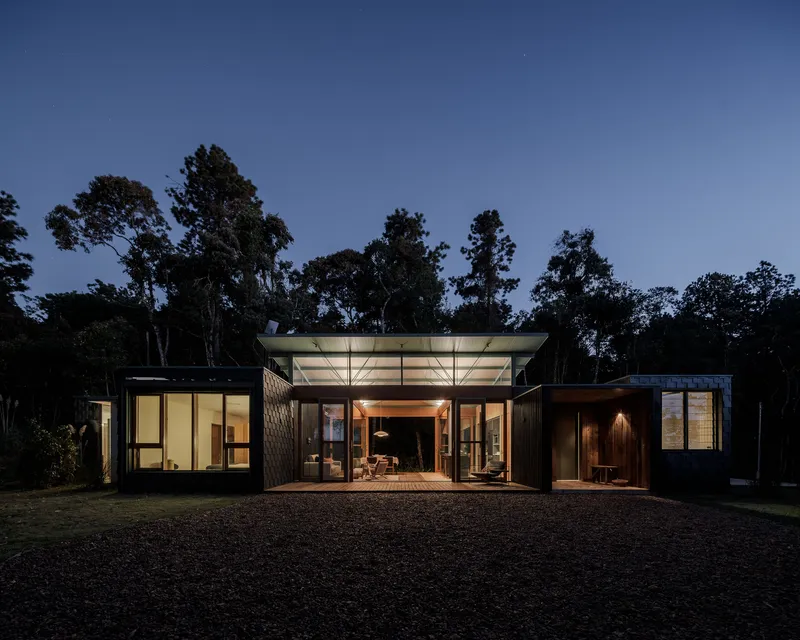 Evening view of the flat-roofed residence with illuminated interiors framed by glass walls and dark cladding panels