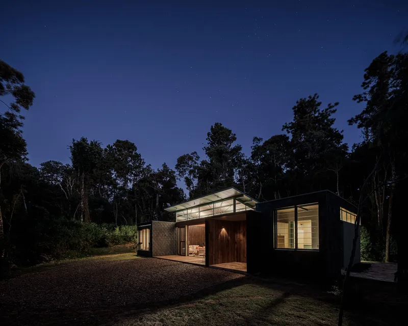 Night view showing the pavilion-roofed central volume flanked by glazed wings against silhouetted trees and starlit sky