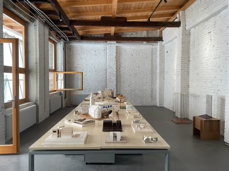 Interior studio space with white painted brick walls, exposed timber ceiling and architectural models on a central table