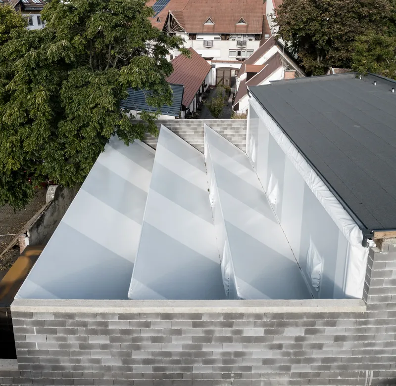 Aerial view of sawtooth skylight structure with white translucent panels atop a patterned brick parapet wall