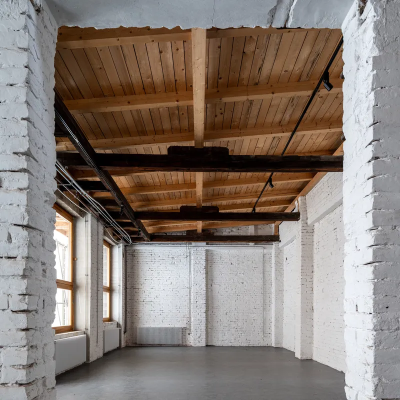 White painted brick interior room with exposed timber plank ceiling and dark steel beams spanning overhead