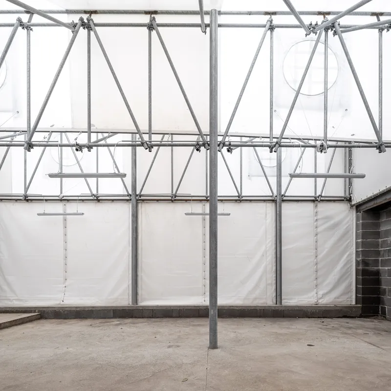 Interior courtyard with galvanized scaffolding frame supporting white tarp enclosure under diffused daylight