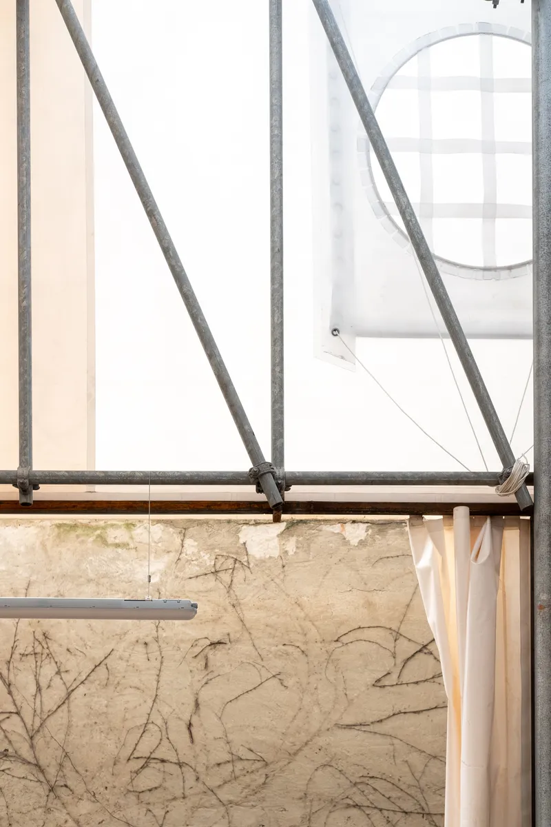 Detail of diagonal steel bracing meeting horizontal rail against weathered plaster wall with visible cracks