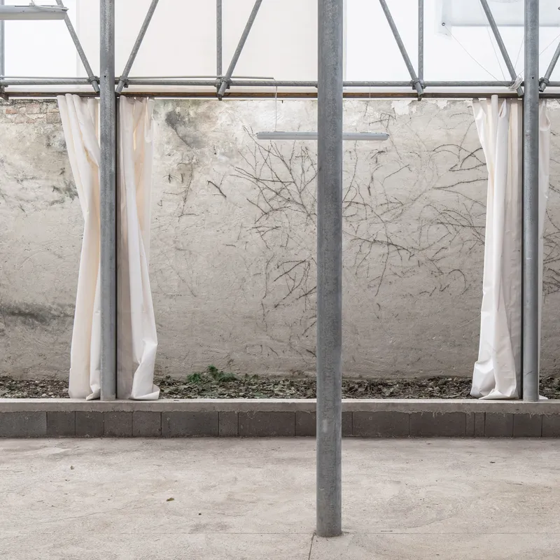 Scaffolding framework with cream fabric curtains suspended along cracked plaster wall on concrete base