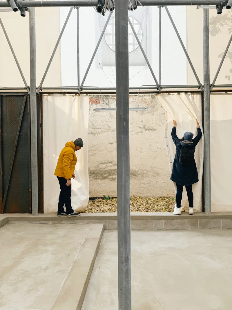 Interior courtyard with steel frame and draped fabric partitions as two visitors arrange the curtains