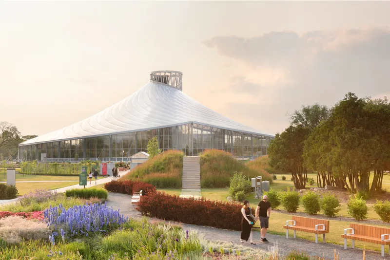 White tensile roof rising to a central lantern above a glass pavilion surrounded by planted beds with visitors