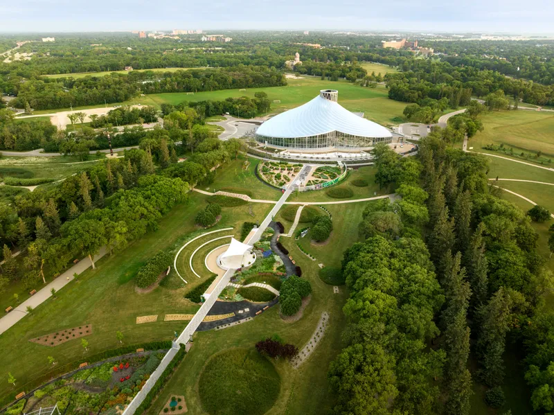 Aerial view of the conical glass conservatory within curved garden paths surrounded by parkland and forest