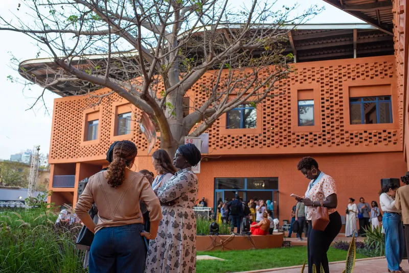 Visitors gather in the courtyard beneath the perforated brick facade and bare branches of the tree