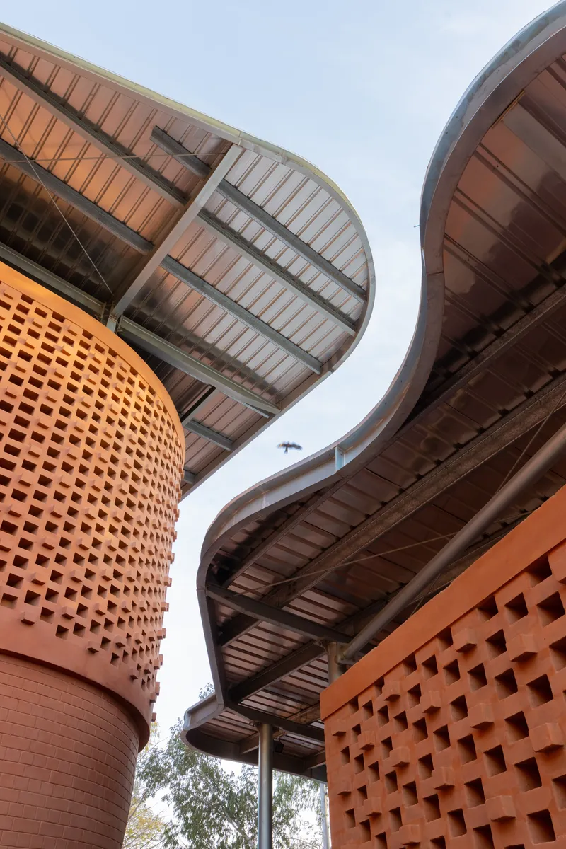 Upward view of perforated terracotta cylindrical volume meeting curved roof canopies with exposed timber soffits