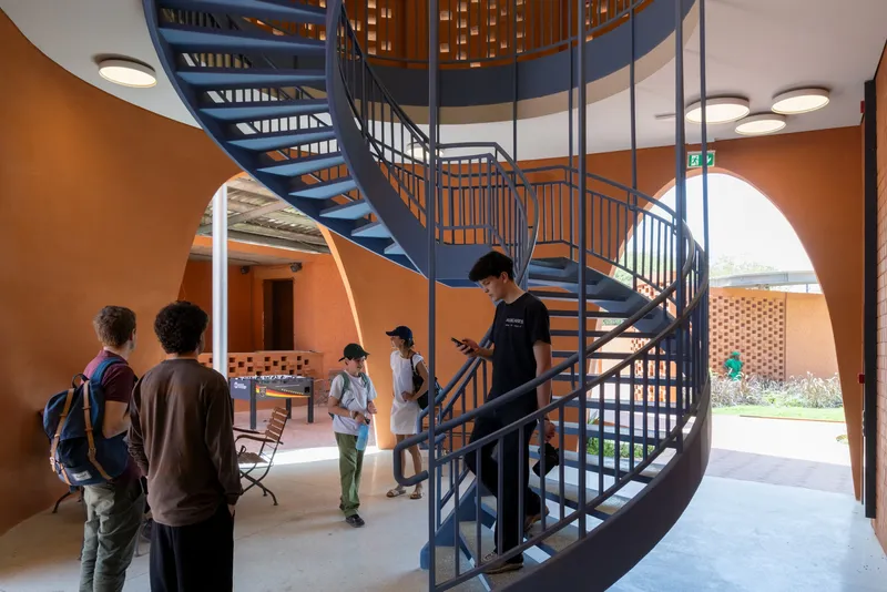 Central spiral staircase with steel railings and visitors gathering on terrazzo floor below round skylights