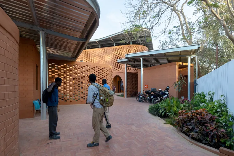 Courtyard entry with perforated brick walls and visitors walking on patterned pavers beside planted beds