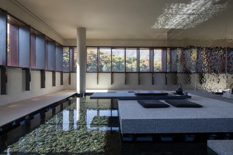 Interior reflecting pool with raised seating platforms beneath glazed clerestory and dappled light on the ceiling
