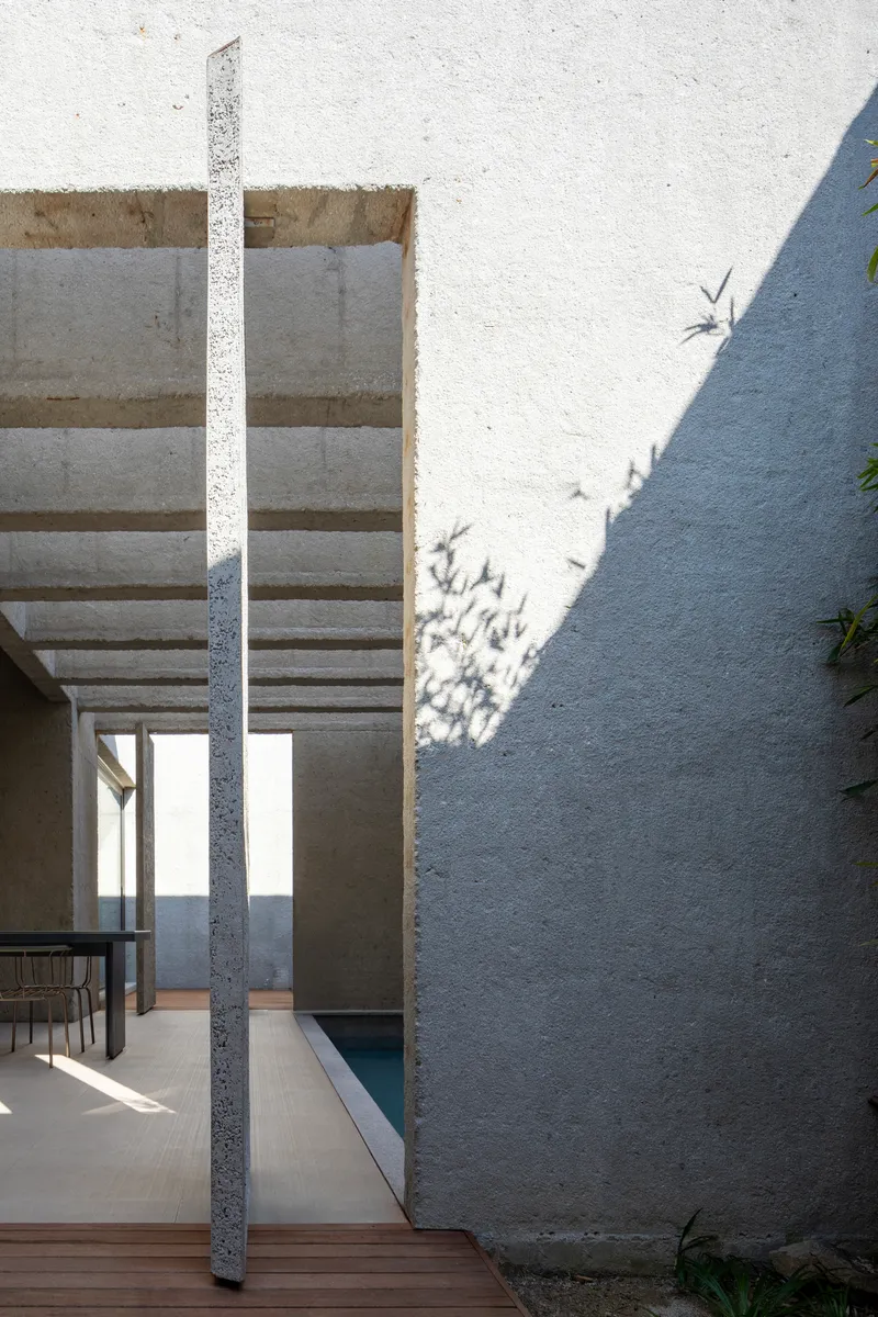 View through a slatted concrete pergola casting crisp shadows on a white textured wall