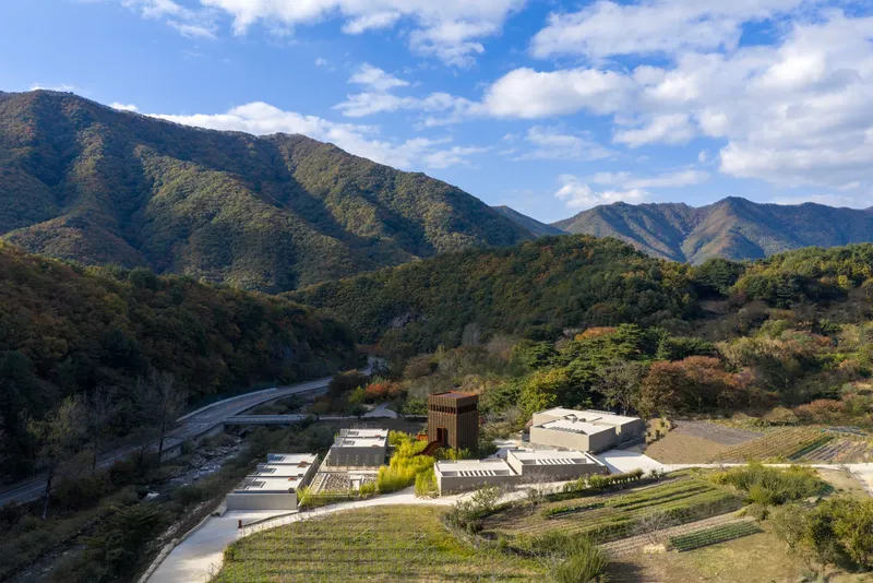 Aerial view of the compound nestled in a mountain valley with terraced gardens and a winding river below