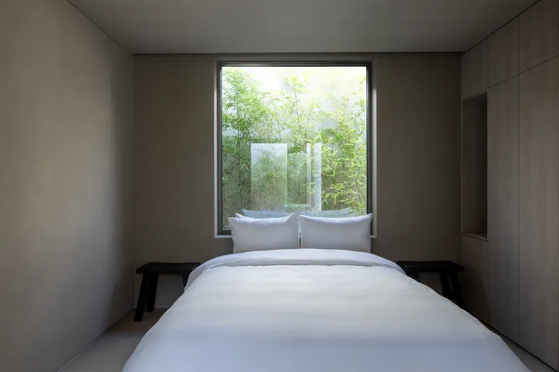 Bedroom with timber-lined walls and window framing a planted courtyard with translucent glass screen