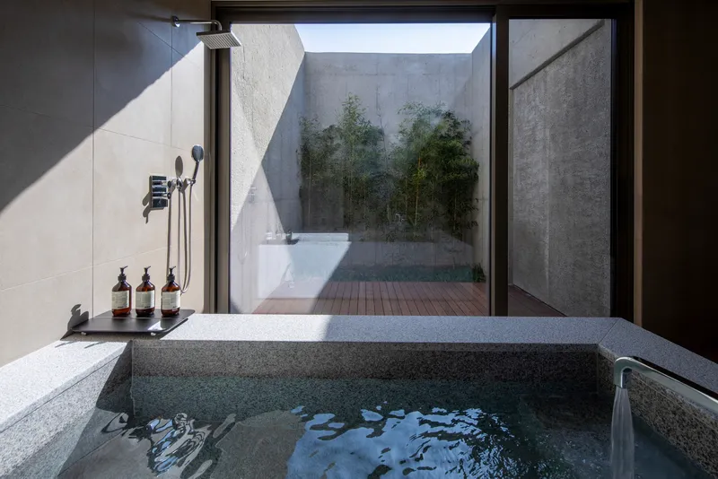 Sunken stone bathtub with rain shower facing a private courtyard with bamboo through floor-to-ceiling glass