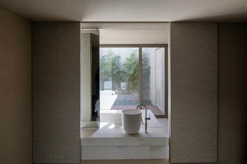 Terrazzo basin and freestanding tub framed by textured wall panels overlooking a courtyard in soft daylight