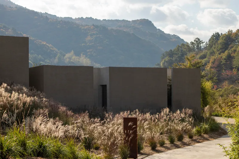 Concrete volumes with door openings set among native grasses with mountains and clouds in the background