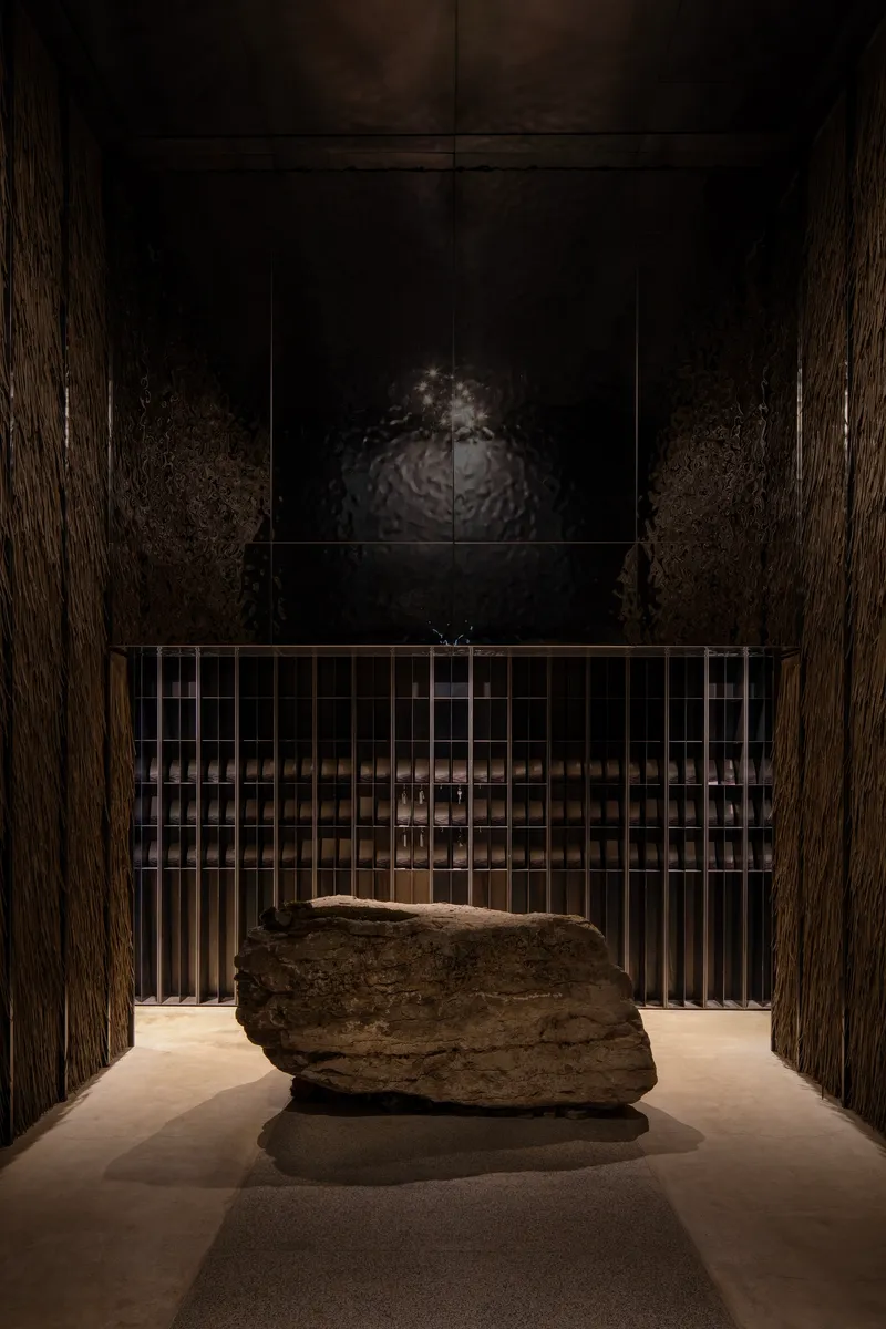 Entry hall with large stone boulder on plinth behind metal grille and dark wood paneling