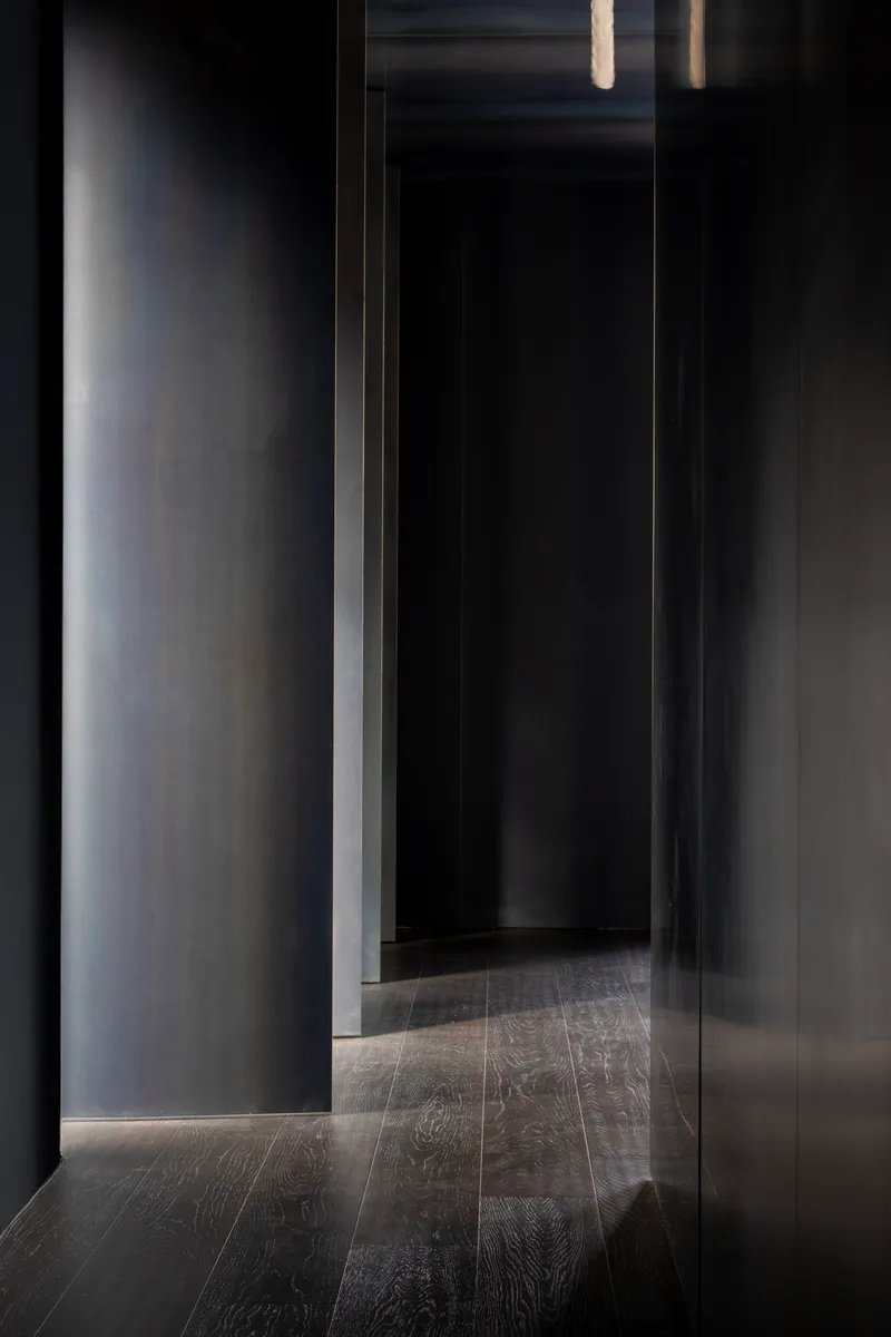 Narrow corridor with dark timber flooring and grey plastered walls lit by recessed strip lighting