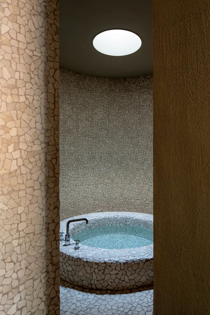 View through curved wall opening toward stone-clad soaking tub beneath circular ceiling skylight