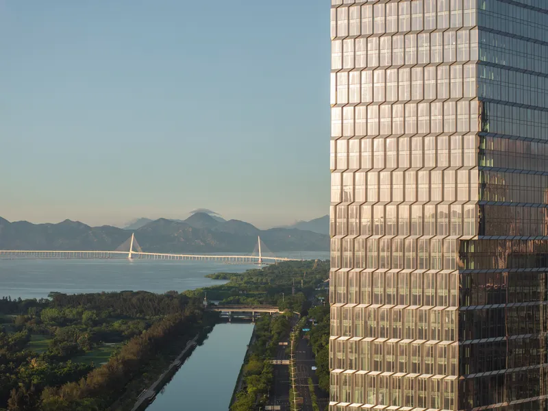 Close-up of gridded glass facade overlooking waterway with cable-stayed bridge and distant mountains