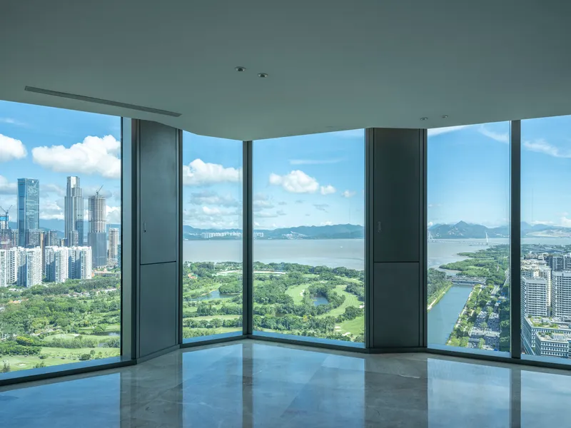 Corner window interior with floor-to-ceiling glass overlooking a golf course and waterfront on a cloudy day