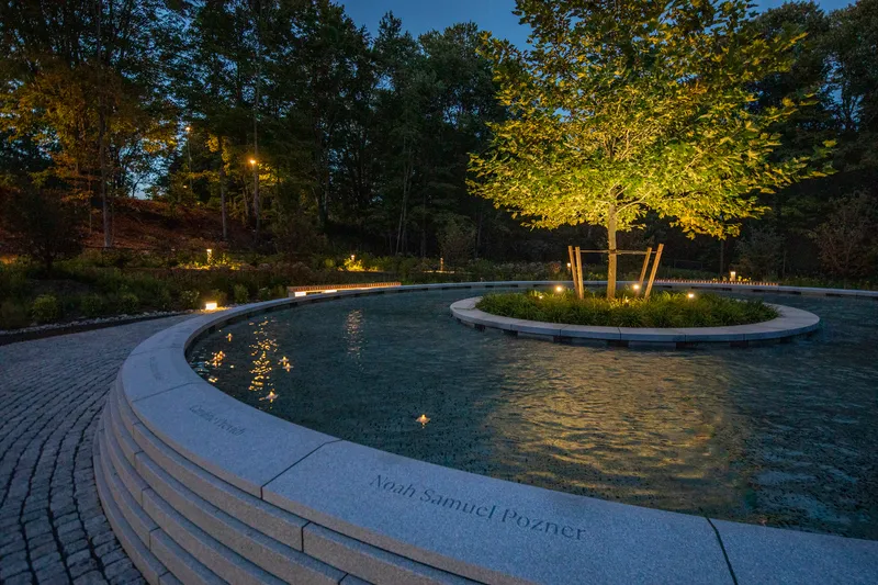 Evening view of the illuminated fountain pools with inscribed coping and lit perimeter planting