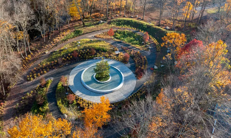 Drone view showing the concentric stone paving rings and curved planted beds in fall color
