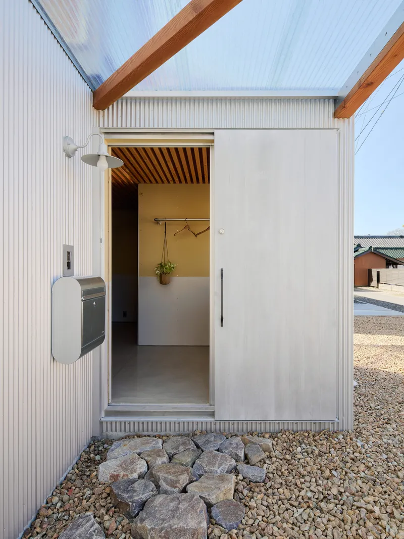 Entrance threshold with corrugated metal cladding and gravel ground beside a mailbox and stone border