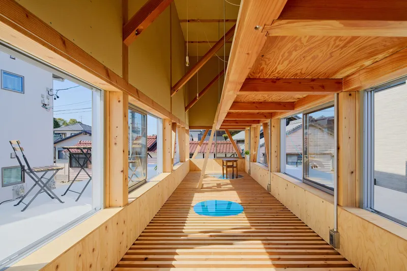 Long timber corridor with slatted floor and exposed diagonal beams casting sunlight stripes through windows