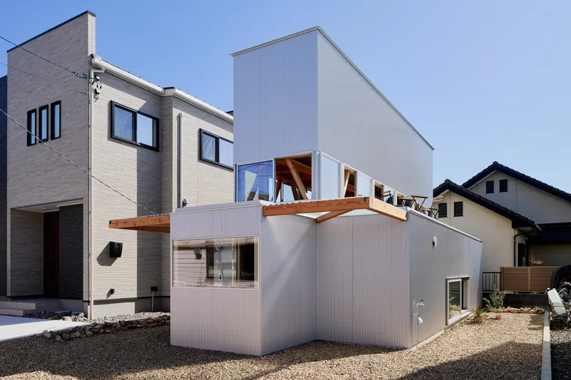 Corrugated metal facade with gravel yard and neighboring houses visible on both sides