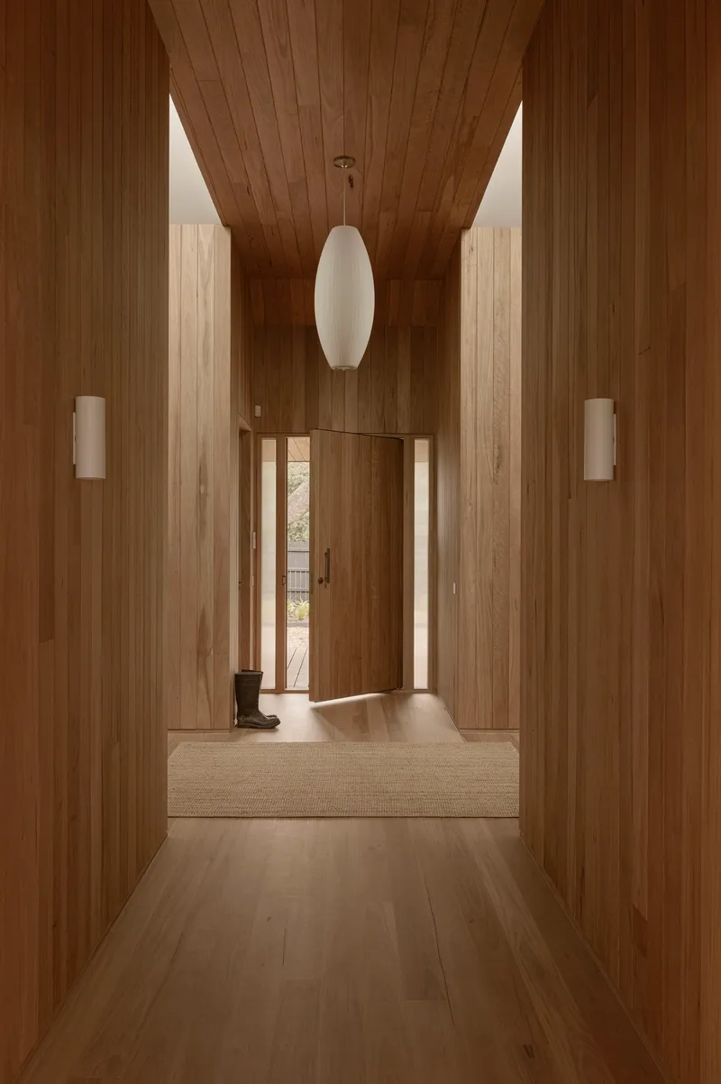 Timber-clad hallway with vaulted ceiling and white pendant light leading to an open entrance